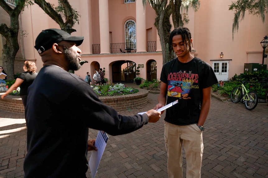 African American man handing out how to vote flyer to young Black college student.