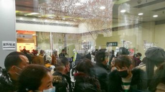 People stand outside a building wearing surgical masks.