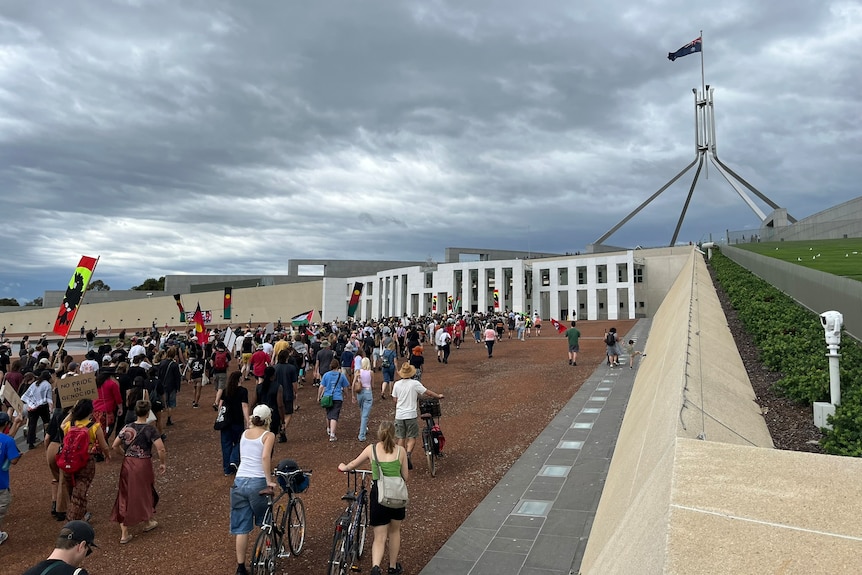 A crowd of people marching to Parliament House on Australia Day 2024 holding signs and flags. 