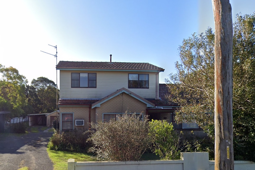 A two-storey fibro house with trees in front of and beside it