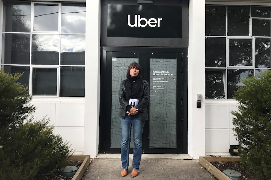 Uber driver Deb standing at a protest outside the company's Melbourne office with sign in the background.