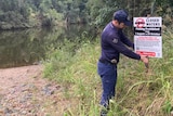 A man in uniform straightens up a sign warning people not to fish here.
