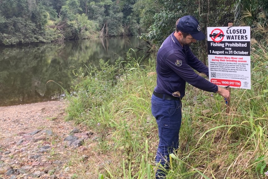 A man in uniform straightens up a sign warning people not to fish here.