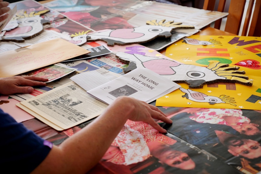 Colourful posters, photos and cockatoo cardboard cut outs scattered on a table with a hand sorting them