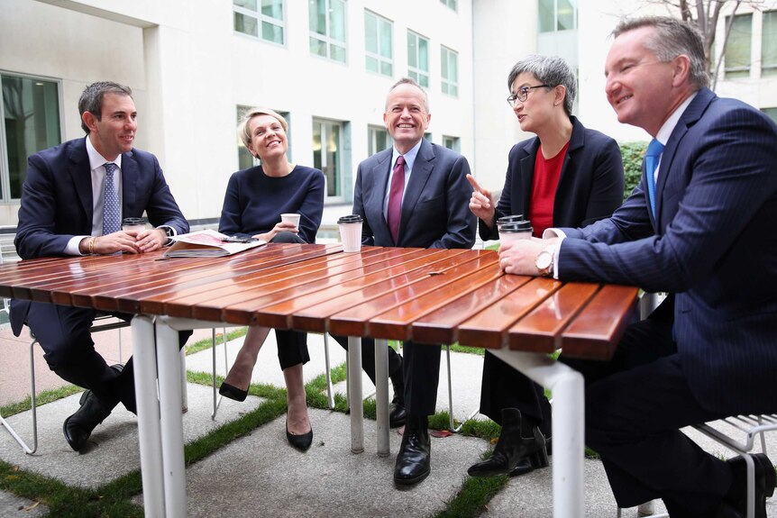 A group of five smiling Labor politicians sit around a table, all holding disposable coffee cups. Penny Wong points a finger.