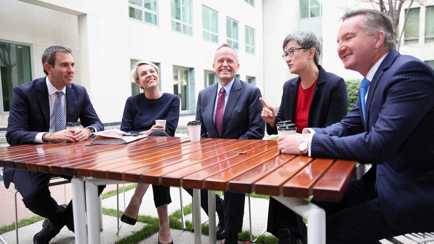 A group of five smiling Labor politicians sit around a table, all holding disposable coffee cups. Penny Wong points a finger.