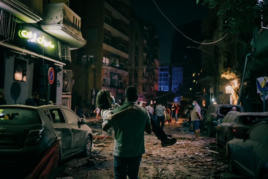 A woman is carried to safety in a street strewn with rubble.