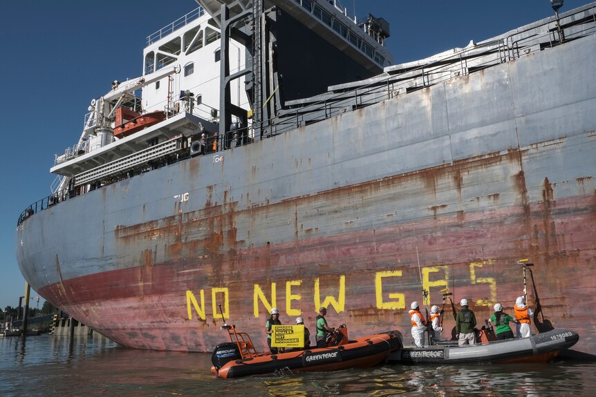 Protesters on a dinghy paint 'no new gas' in yellow on the side of a large ship