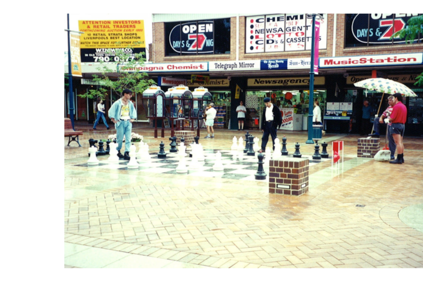 A life size chess set from the 1990s with two men standing around ready to play