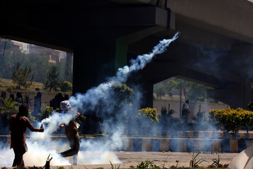 Trajectory of smoke visible as person throws tear gas cannister.