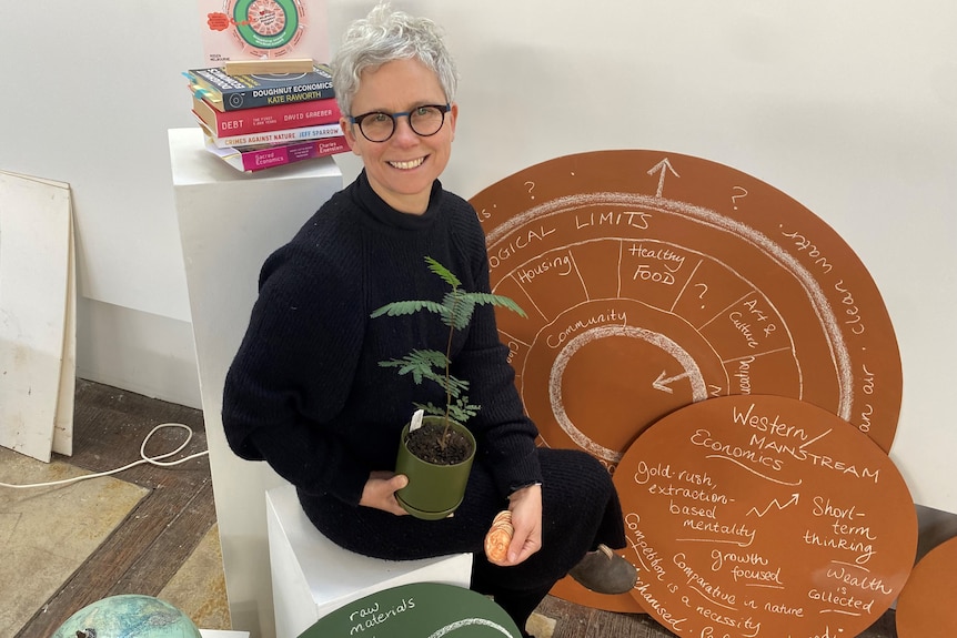 woman sitting holding a silveyr wattle plants and coins in her hand, smiling