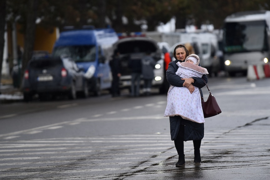 A woman walks down a street clutching a small child in her arms.