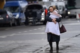 A woman walks down a street clutching a small child in her arms.