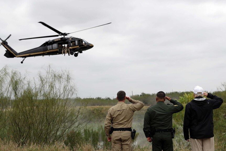 Three men, including Donald Trump, salute a customs helicopter flying low.