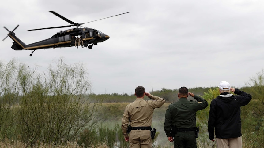 Three men, including Donald Trump, salute a customs helicopter flying low.