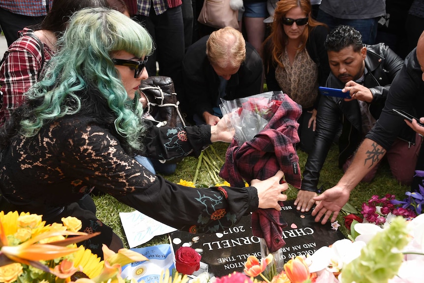 A fan leaves roses wrapped in a plaid shirt at the gravesite of the late singer Chris Cornell.