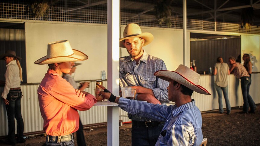 Three people in button up shirts, blue jeans and cowboy hats share a drink.