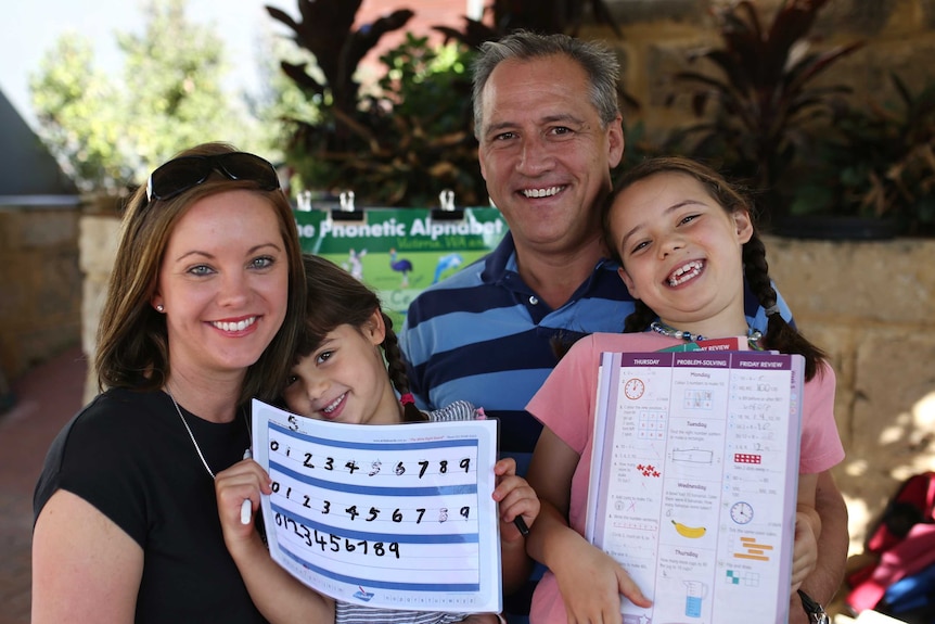 Mikki and Keith Williams with their daughters Hallie and Charlotte, who are holding up some home schooling work.