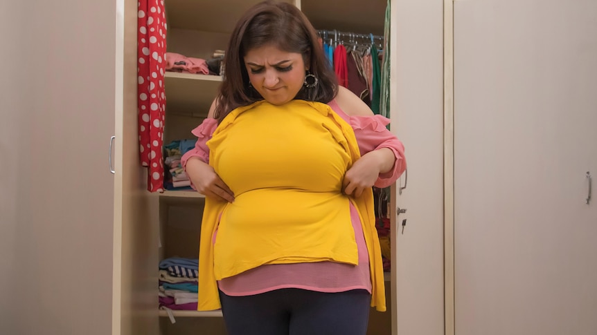 A woman holds a top against her body while standing in front of a wardrobe.