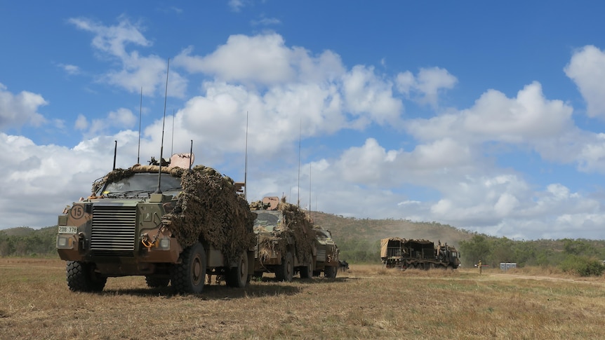Army tanks driving in a paddock under a blue sky.