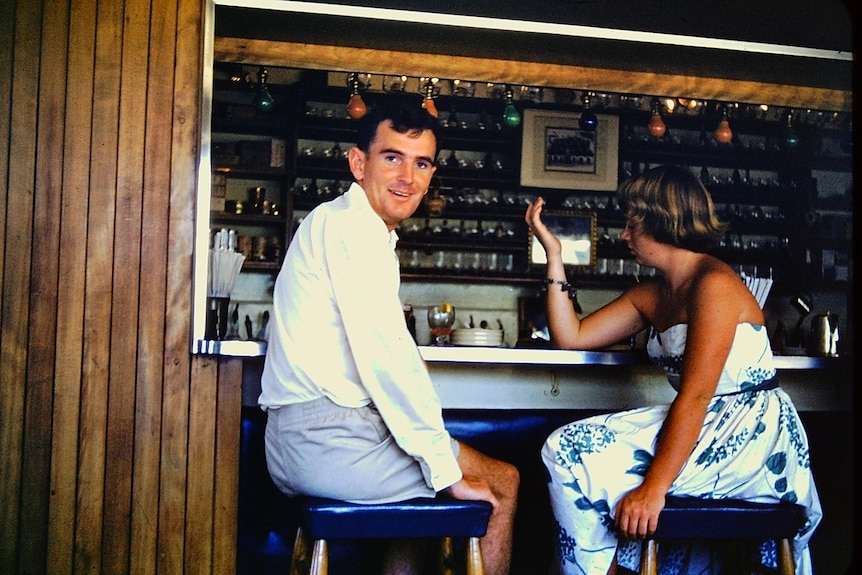 An old photo of a young John Gorman sitting on a stool at a cruise ship bar in the 1950s