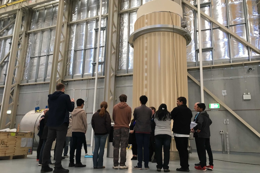 A group of people look at the TN81 cask that currently holds nuclear waste.