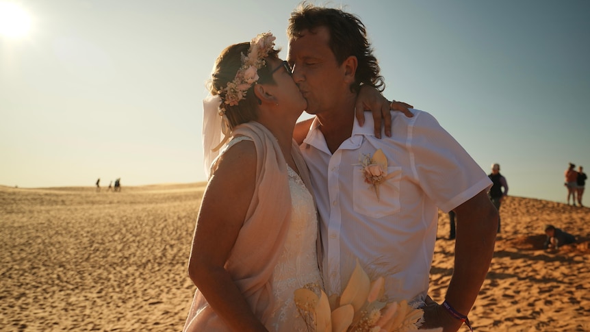 Woman and man kissing on sand dune