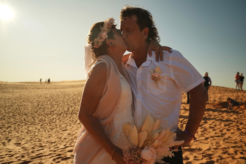 Woman and man kissing on sand dune
