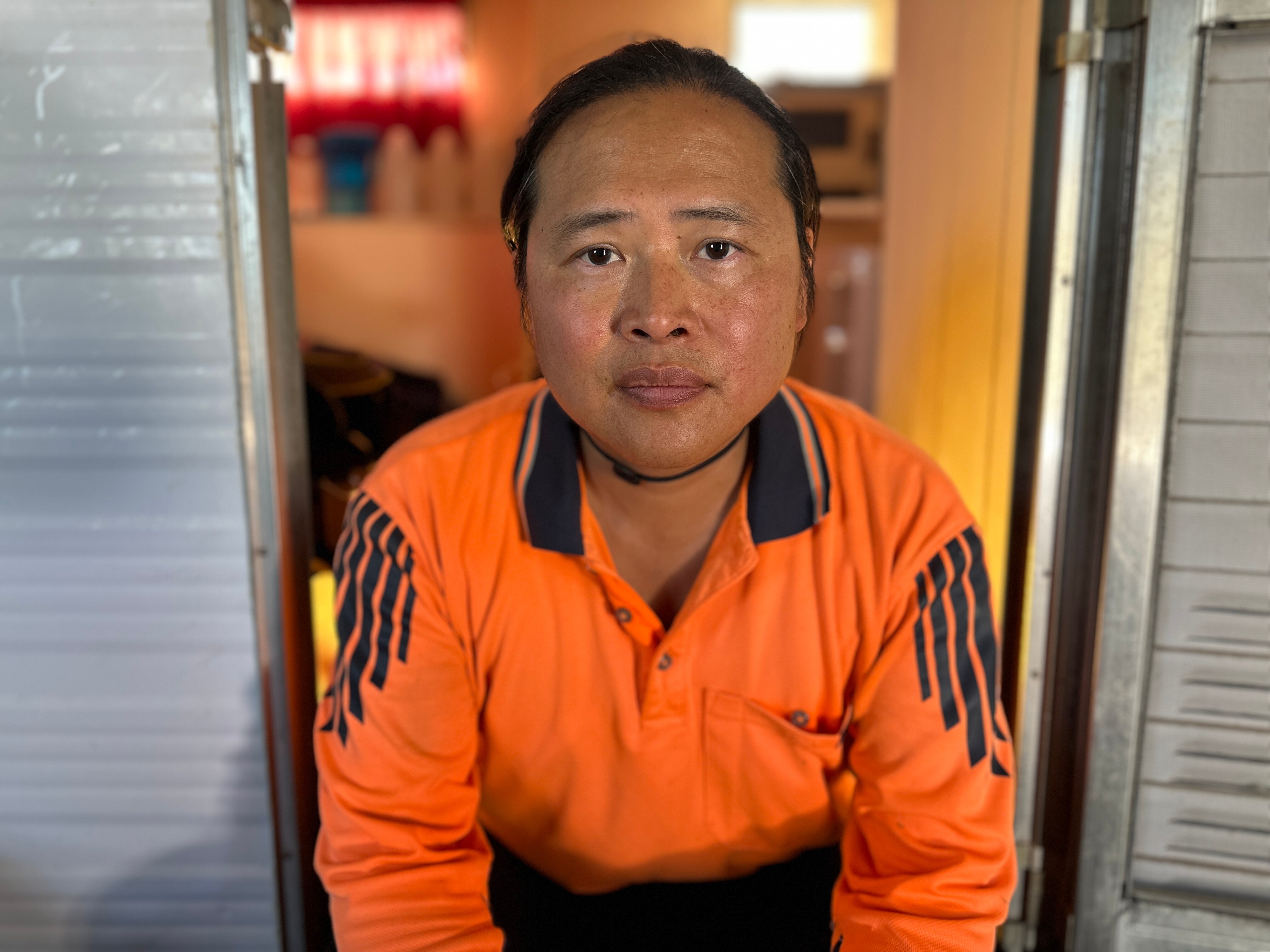 A man poses for a photo in a doorway wearing a high-vis orange work shirt