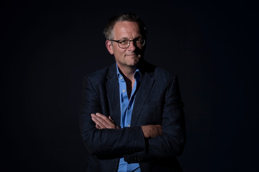 Michael Mosley smiles for a portrait with his arms crossed in front of a dark backdrop