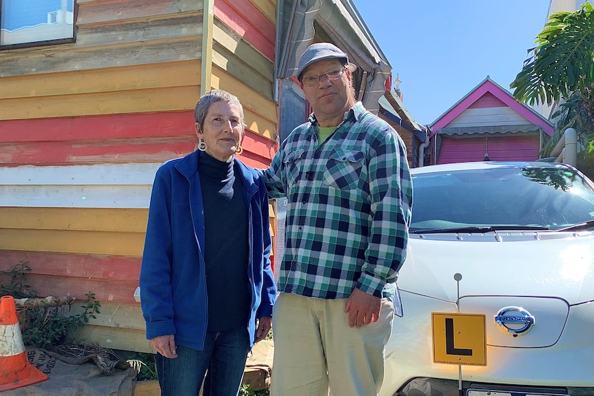 A man and a woman stand in front of a car.