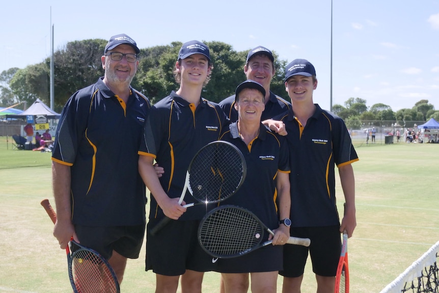 family standing with rackets on tennis court
