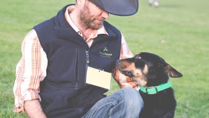 Working dog Glencairn Seven sitting next two owner and trainer Christian Peackock on the grass.