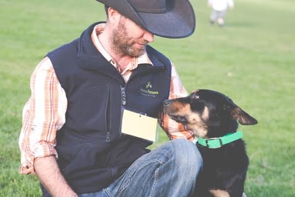 Working dog Glencairn Seven sitting next two owner and trainer Christian Peackock on the grass.