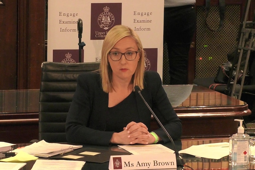 a woman wearing glasses looking and sitting behind a desk