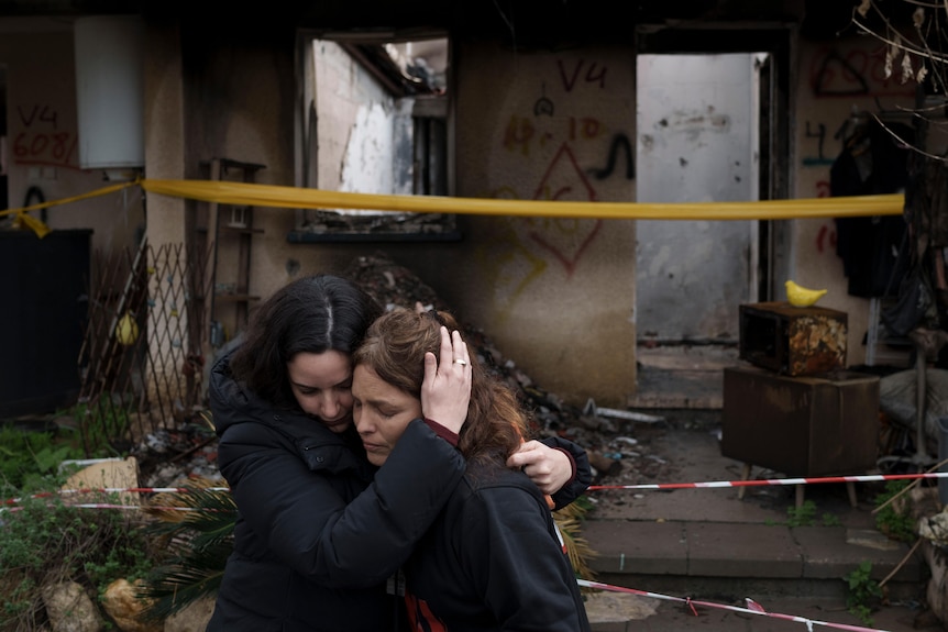 Two women embrace outside a burnt building. 