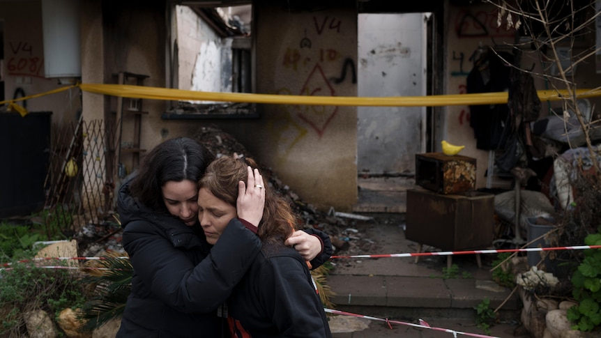 Two women embrace outside a burnt building. 