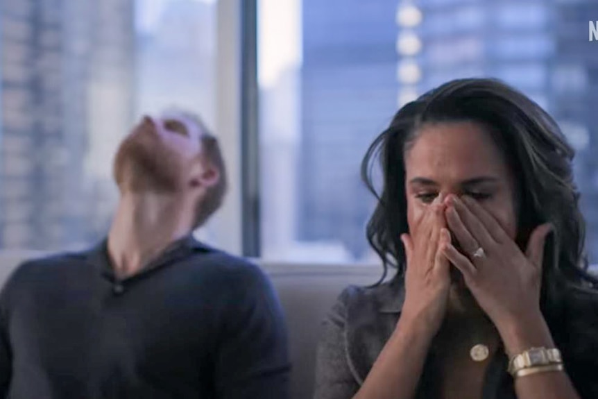 Meghan Markle wipes her eyes while Prince Harry rests his head on the a couch