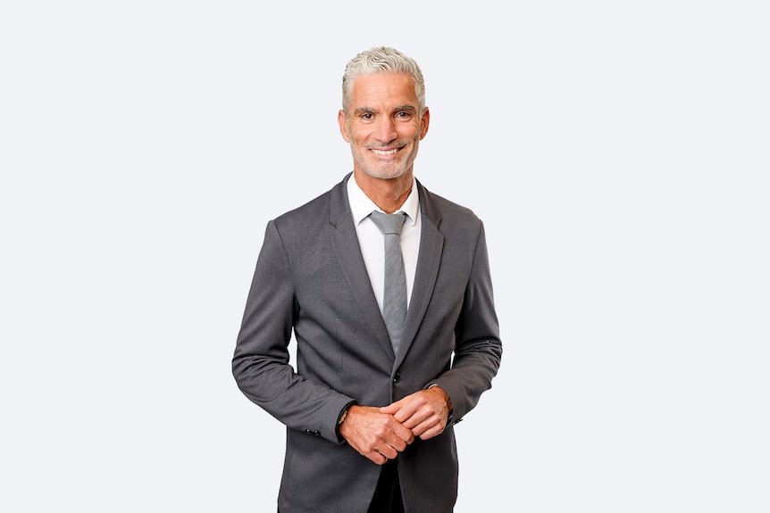 Craig Foster is a man with pale skin and short, grey hair. He is wearing a grey suit with a grey tie.