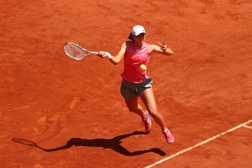 Iga Swiatek stretches for a shot on a clay court.