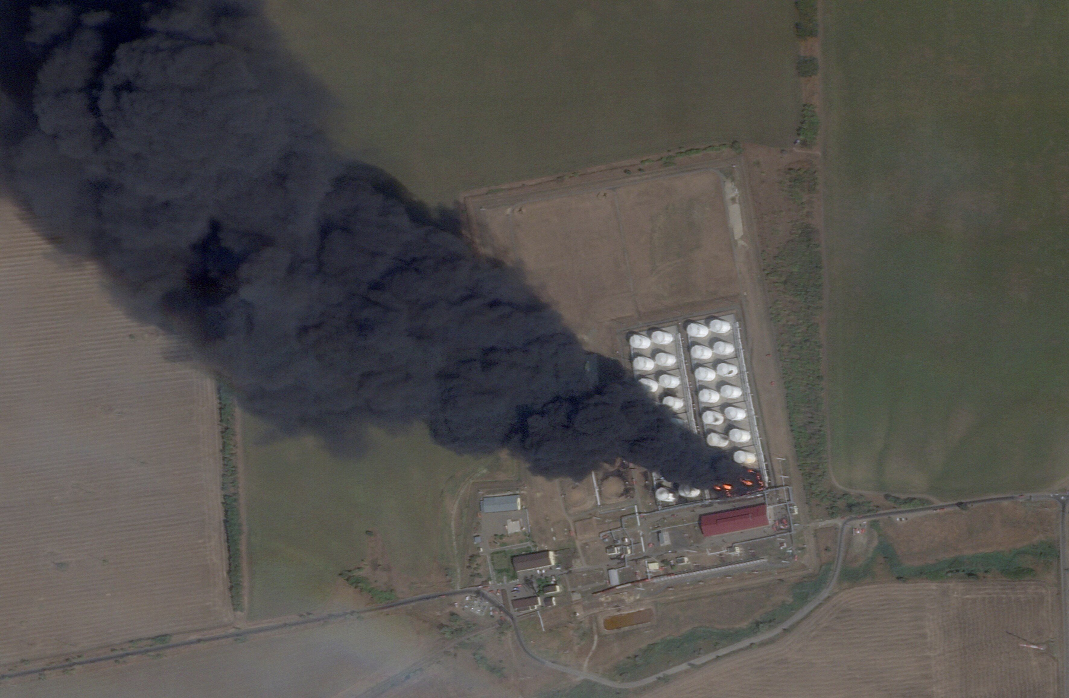 A satellite image shows smoke and fire rising from an oil depot.