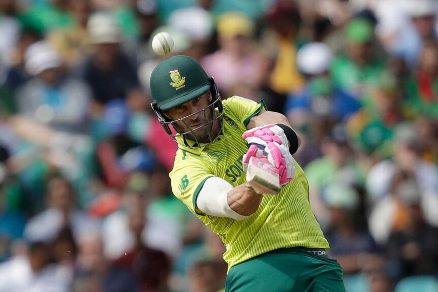 Faf du Plessis holds his cricket bat in both hands and hits a ball upwards towards the camera