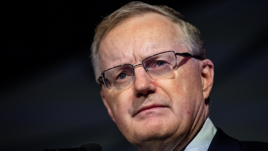 A close shot of Reserve Bank of Australia Governor Philip Lowe wearing a suit against a dark background.