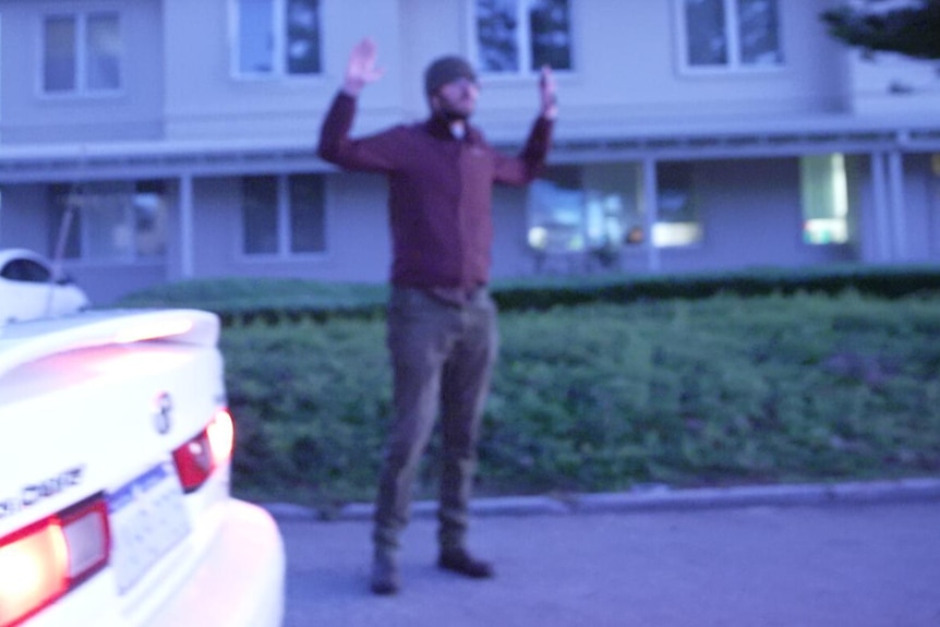 A man raising his arms next to a car. 