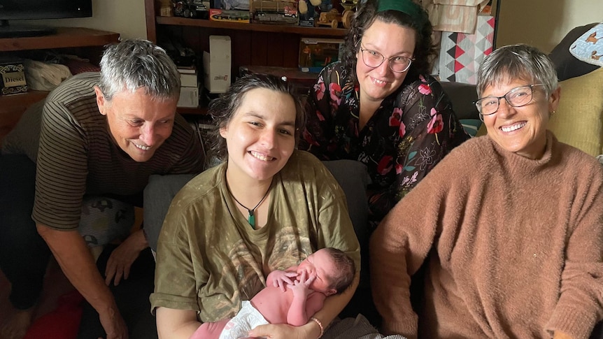 A young mum holding a newborn baby, with three other women around her.