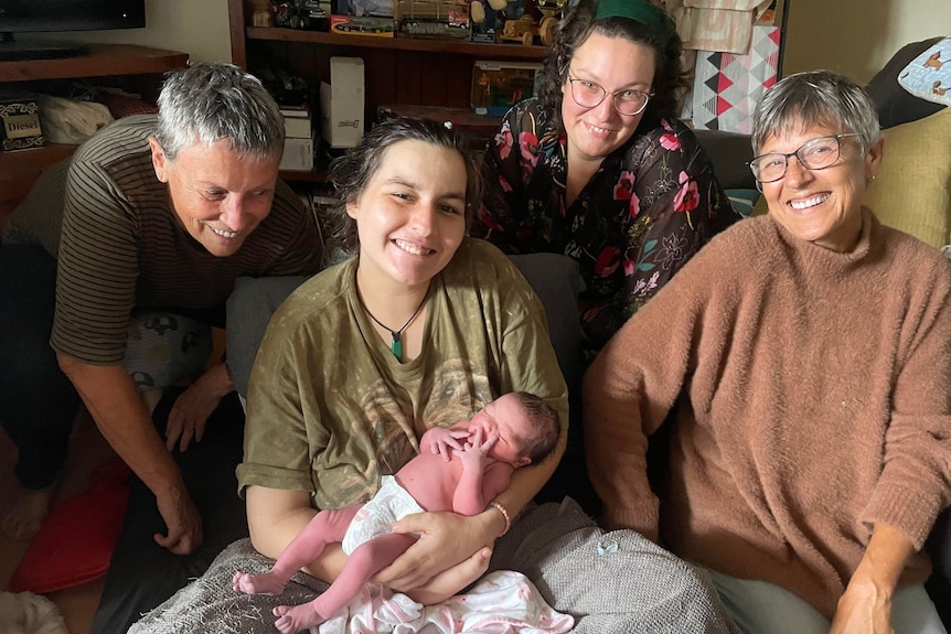 A young mum holding a newborn baby, with three other women around her.