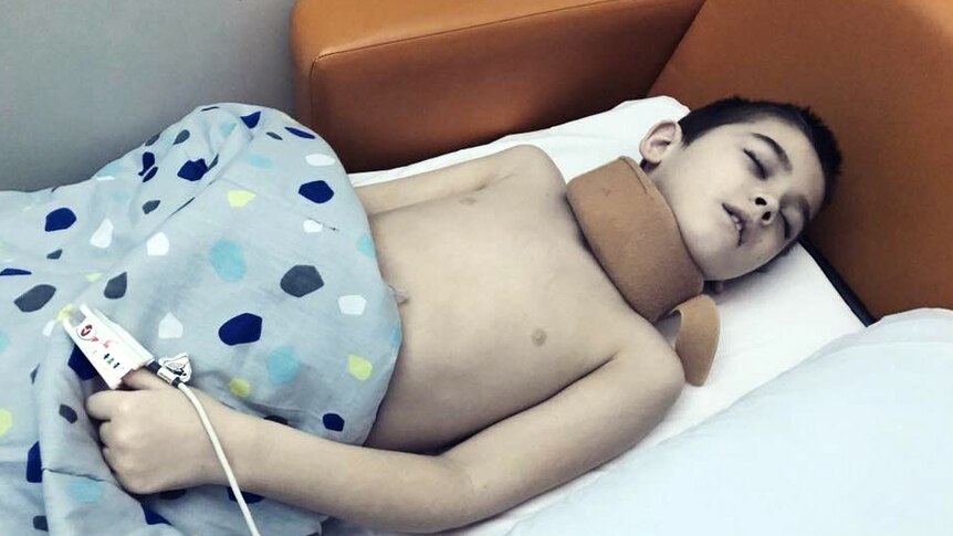 Eight year old boy lays in a hospital lounge, sleeping.