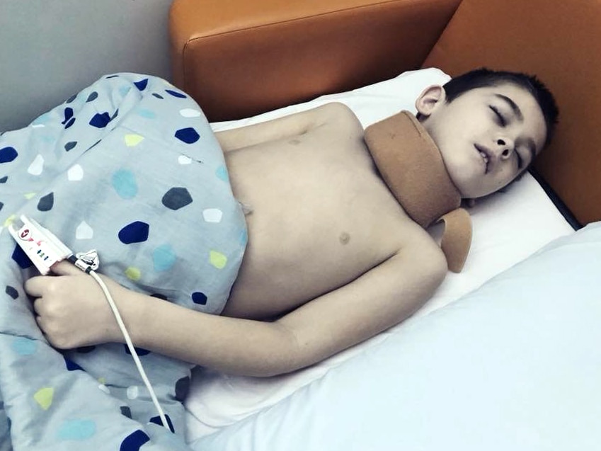 Eight year old boy lays in a hospital lounge, sleeping.