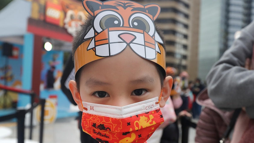 A boy wears a hat in the shape of a tiger and a Lunar New Year-patterened face mask.