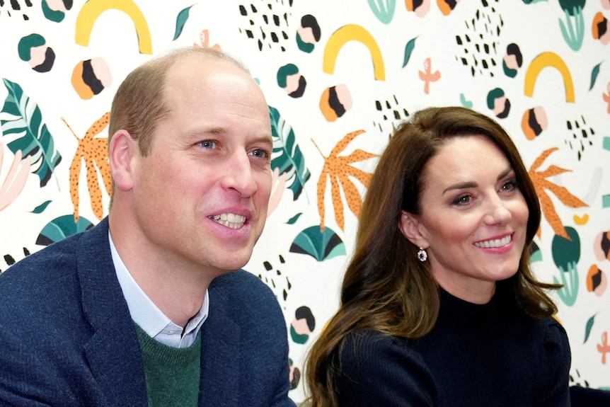 Kate, Princess of Wales, and Prince William smile as they sit in front of bright wallpaper.